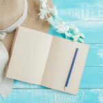 How to coordinate hats and clothes to stay on trend A creative flat lay featuring a straw hat, a blank notebook, and a pencil on a blue wooden surface.