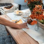 Host setting a wine glass on an autumn dinner table with orange flowers